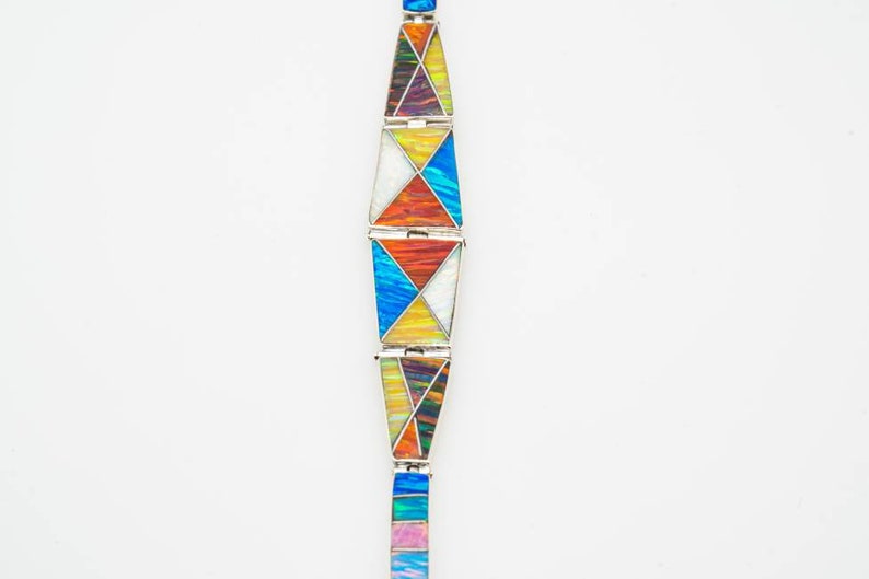 May include: A silver bracelet with geometric shapes in various colors, including blue, orange, yellow, and white. The bracelet is made of multiple connected segments, each with a unique pattern. The background is plain white.
