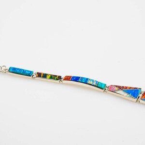 May include: A silver bracelet with a geometric design made of colorful opal stones. The bracelet is made up of rectangular and triangular shapes.