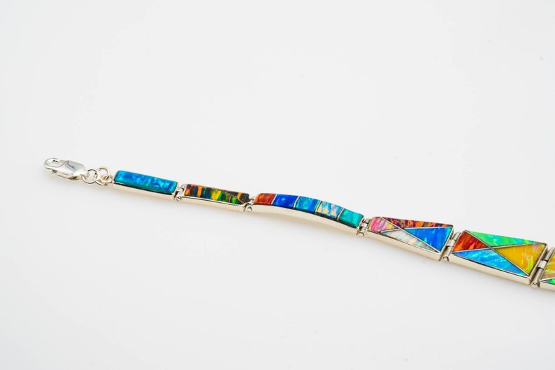 May include: A silver bracelet with a geometric design made of colorful opal stones. The bracelet is made up of rectangular and triangular shapes.