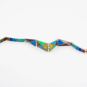 May include: A colorful bracelet made of inlaid stone and silver. The bracelet is made up of rectangular and triangular pieces of stone, each with a different pattern and color. The bracelet is open and has a clasp.