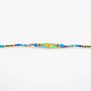 May include: A silver bracelet with a geometric design made of colorful inlaid stones. The stones are arranged in a pattern of triangles and rectangles.