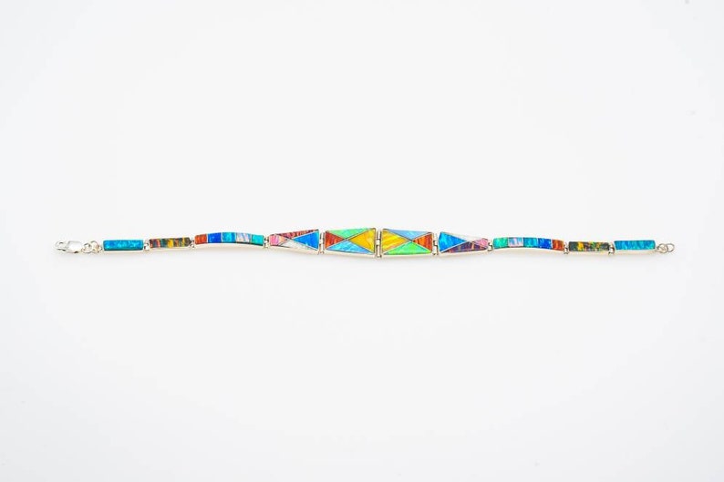 May include: A silver bracelet with a geometric design made of colorful inlaid stones. The stones are arranged in a pattern of triangles and rectangles.