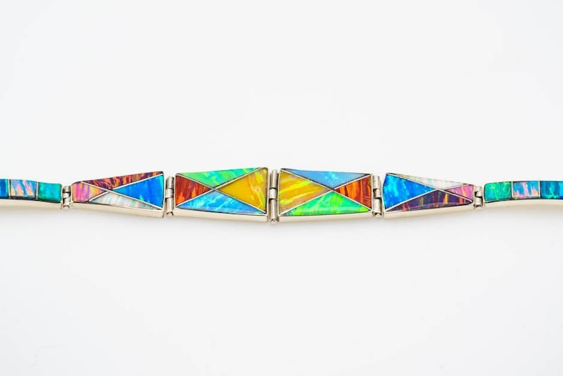 May include: A colorful bracelet made of inlaid opal and silver. The bracelet is made up of five triangular sections, each with a different pattern of opal.