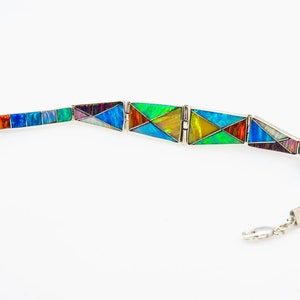 May include: A silver bracelet with a geometric design made of colorful opal stones. The bracelet is made of individual pieces that are connected by a silver chain.