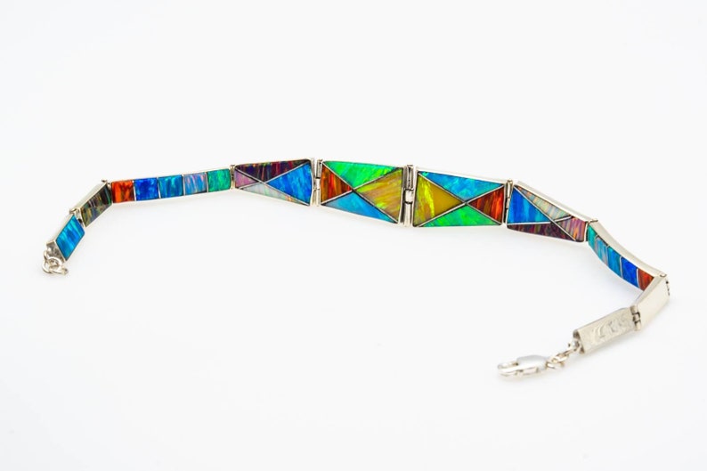 May include: A silver bracelet with a geometric design made of colorful opal stones. The bracelet is made of individual pieces that are connected by a silver chain.