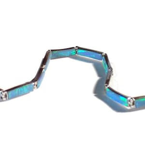 May include: A silver bracelet with blue opal links. The bracelet is made of rectangular links that are connected together. The opal is a light blue color with green and iridescent flashes.