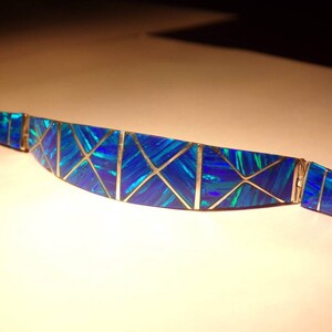 May include: A blue and silver opal bracelet with a geometric design. The bracelet is made of small pieces of opal that are set in silver.