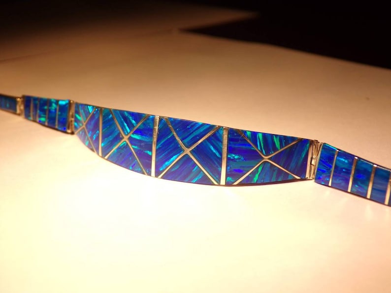 May include: A blue and silver opal bracelet with a geometric design. The bracelet is made of small pieces of opal that are set in silver.