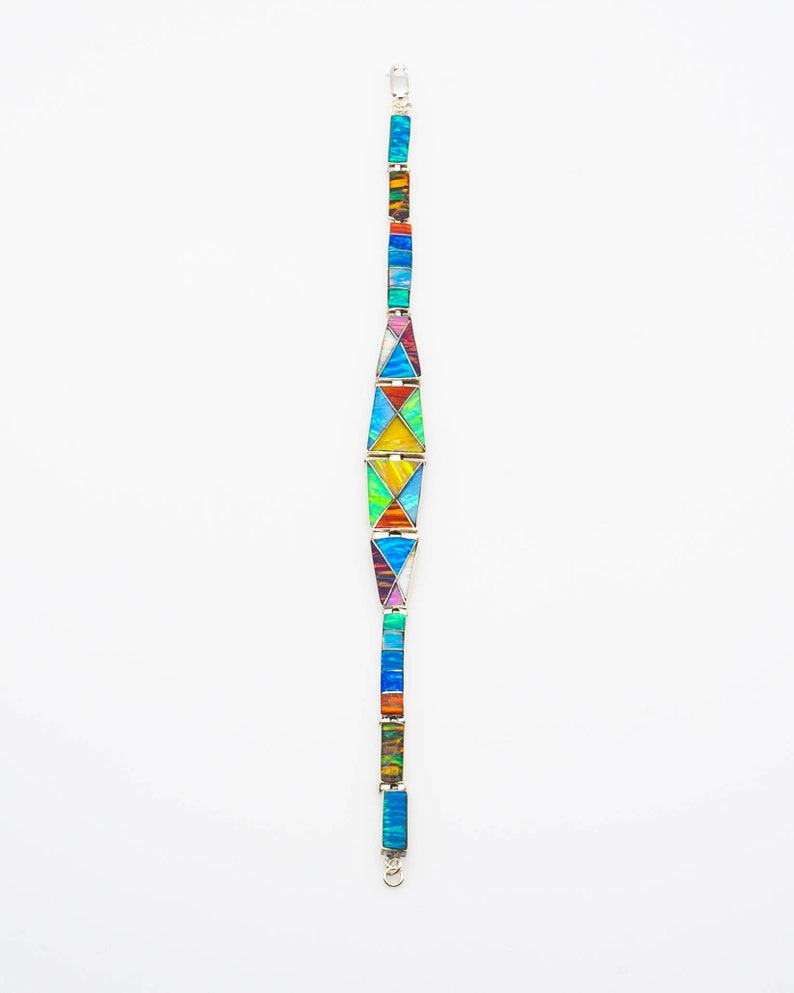 May include: A colorful bracelet with a geometric design made of inlaid opal and silver. The bracelet is made up of a series of triangles and rectangles, each with a different color of opal.