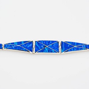 May include: A silver bracelet with blue opal inlay. The bracelet is made of multiple sections that are connected by hinges. The opal is cut into geometric shapes and set in silver.