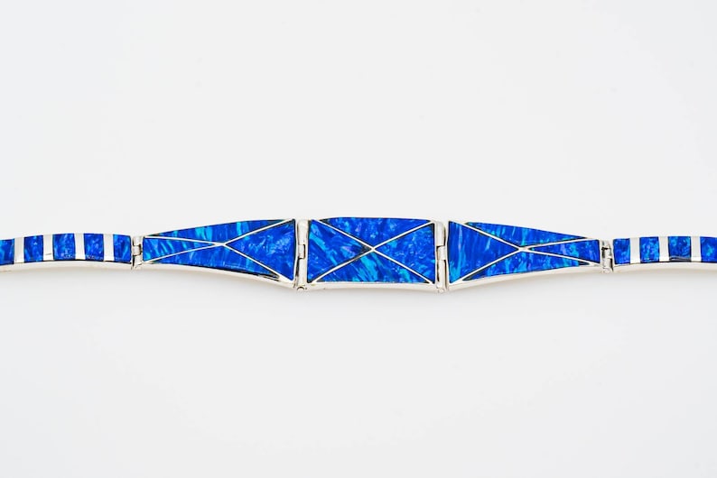May include: A silver bracelet with blue opal inlay. The bracelet is made of multiple sections that are connected by hinges. The opal is cut into geometric shapes and set in silver.