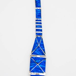 May include: A silver bracelet with blue opal stones set in a geometric pattern. The bracelet is made of multiple sections that are connected together.