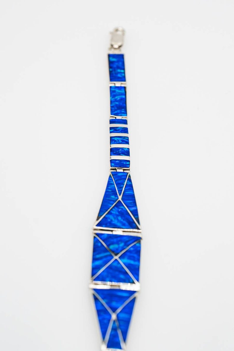 May include: A silver bracelet with blue opal stones set in a geometric pattern. The bracelet is made of multiple sections that are connected together.