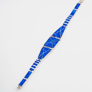 May include: A silver bracelet with blue opal inlay. The bracelet is made of a series of triangular shapes that are connected together.