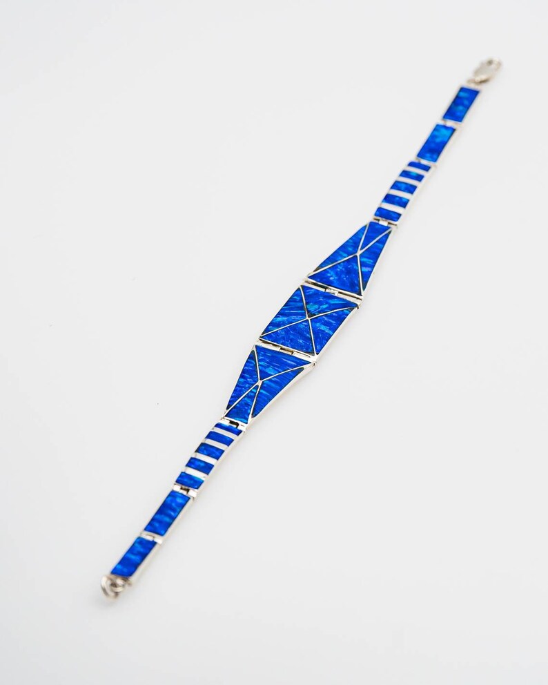 May include: A silver bracelet with blue opal inlay. The bracelet is made of a series of triangular shapes that are connected together.