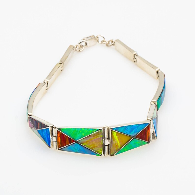 May include: A silver bracelet with a geometric design featuring colorful opal inlay. The bracelet is made up of triangular shaped links.