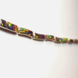 May include: A silver chain bracelet with iridescent opal stones. The stones are set in rectangular shapes and are arranged in a staggered pattern.