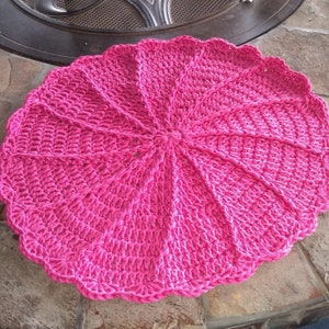 Puede incluir: Una alfombra redonda de crochet rosa con un borde festoneado.