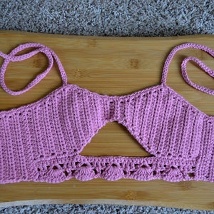Puede incluir: Un top halter de crochet rosa con un diseño de corte y un borde inferior festoneado.