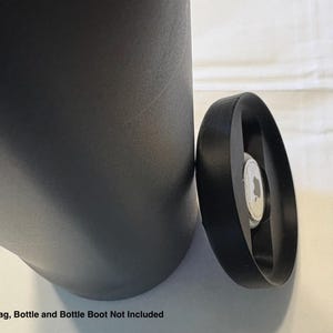 May include: A black bottle boot with a circular design, next to a dark gray bottle. The image includes the text "Airtag, Bottle and Bottle Boot Not Included".