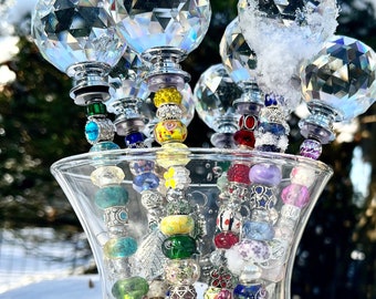 May include: A glass vase filled with colorful glass beads on a string, topped with crystal ball finials. The vase is sitting on a snowy surface.