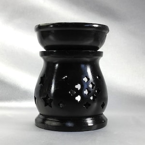 May include: Black ceramic oil burner with a star and heart design. The burner has a removable top bowl for holding wax melts or essential oils.