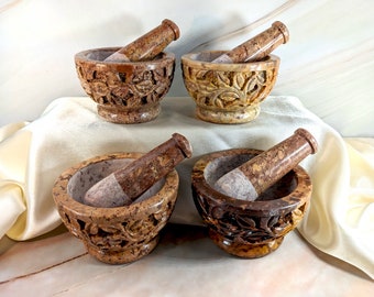 May include: Four carved stone mortar and pestle sets. Each set features a brown and beige mortar with a matching pestle. The mortars have a floral design carved into the sides.