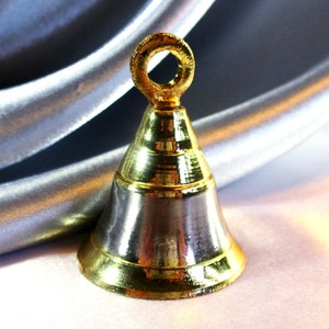 May include: A small gold bell with a silver-colored body and a gold loop at the top. The bell is sitting on a silver fabric background.
