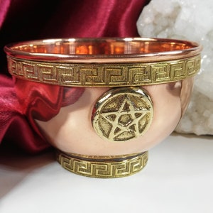 May include: A small copper bowl with a gold pentagram design. The bowl has a decorative gold trim around the top and bottom.