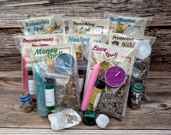 May include: Assortment of spell kits with various components, including candles, herbs, and vials of liquid. Each kit is labeled with a specific intention, such as "Money Spell" and "Love Spell". The kits are arranged on a wooden surface.