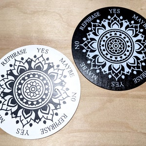 May include: Two black and white circular divination boards with the words "YES", "NO", "MAYBE", and "REPHRASE" printed around the edge. The boards feature a mandala design in the center.