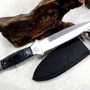 May include: A black and silver knife with a wooden handle and a black leather sheath.