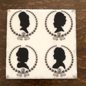 May include: A square, white tile featuring four black silhouette portraits of women within laurel wreaths. Each portrait is framed by a wreath and a decorative bow. The tile has a slightly textured surface.