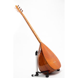 Może przedstawiać: Drewniany turecki saz, instrument strunowy, z perłową powierzchnią, jest prezentowany na czarnym metalowym stojaku na białym tle.