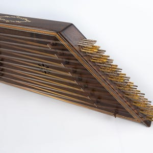 May include: A wooden santur, a hammered dulcimer, with a dark brown finish and gold-coloured tuning pegs. The instrument has a triangular shape and is decorated with intricate inlaid designs.