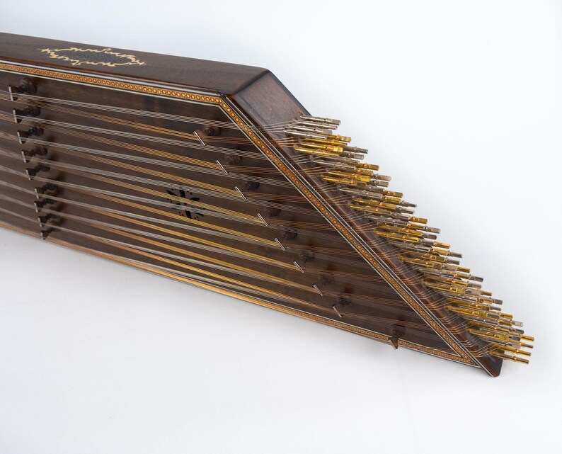 May include: A wooden santur, a hammered dulcimer, with a dark brown finish and gold-coloured tuning pegs. The instrument has a triangular shape and is decorated with intricate inlaid designs.