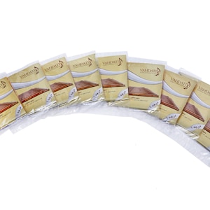 Peut inclure: Un ensemble de 12 paquets individuels de cordes de sitar de la marque "Vahdatti". Chaque paquet est étiqueté avec le nom de la marque et le numéro "12" dans le coin inférieur droit.