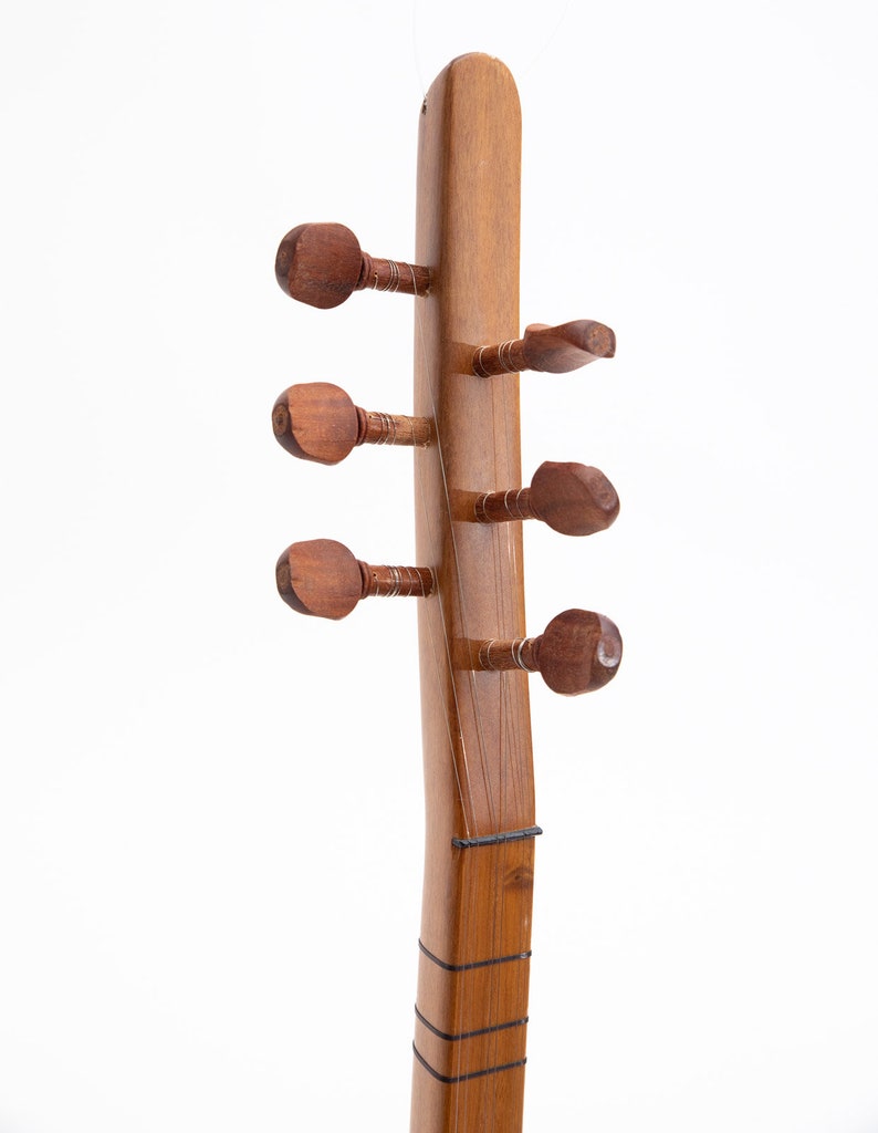 May include: Close-up of the headstock of a wooden stringed instrument. The instrument has six tuning pegs, each with a rounded, carved design. The wood has a warm, brown tone, and the strings are visible along the neck.