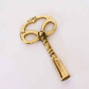 May include: A gold-colored key with a unique heart-shaped design. The key is labeled "KOBE" and "Pr."