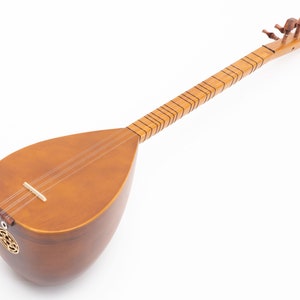 May include: A wooden long-necked stringed instrument, likely a saz or similar folk instrument. The body is a warm brown color, with a pear-shaped soundbox. The neck is long and slender, with frets and tuning pegs. The instrument has three strings and a decorative sound hole.