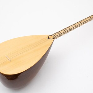 May include: A traditional Turkish stringed instrument called a saz. The saz has a pear-shaped body made of wood and a long neck with frets. The instrument is finished in a natural wood color.