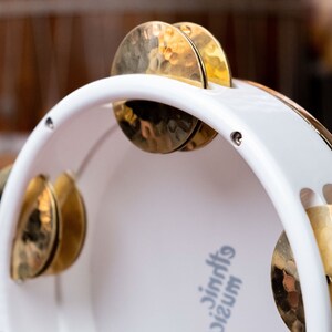May include: White tambourine with gold cymbals. The tambourine has the text "music jingles" printed on the side.