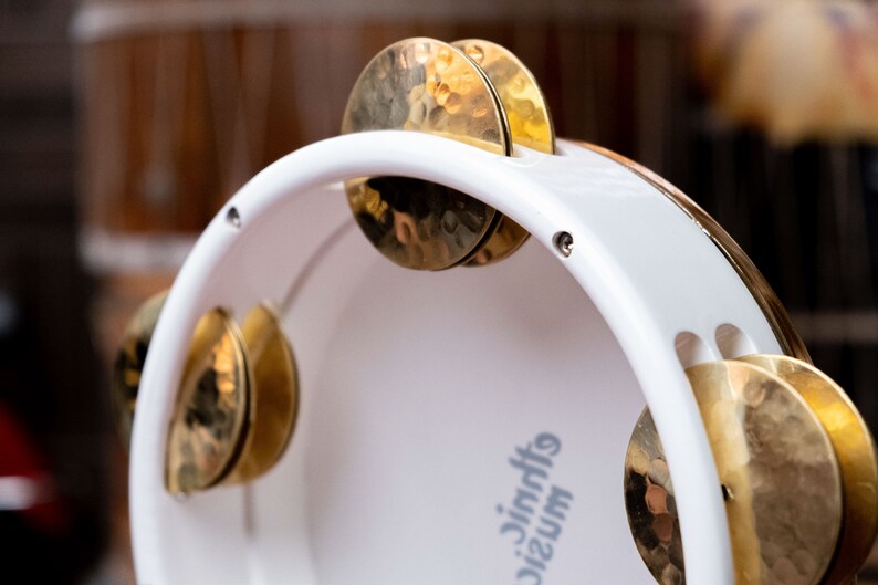 May include: White tambourine with gold cymbals. The tambourine has the text "music jingles" printed on the side.