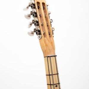 May include: Close-up of the headstock of a wooden stringed instrument with silver tuning pegs. The neck of the instrument has black lines running down the length of the neck.