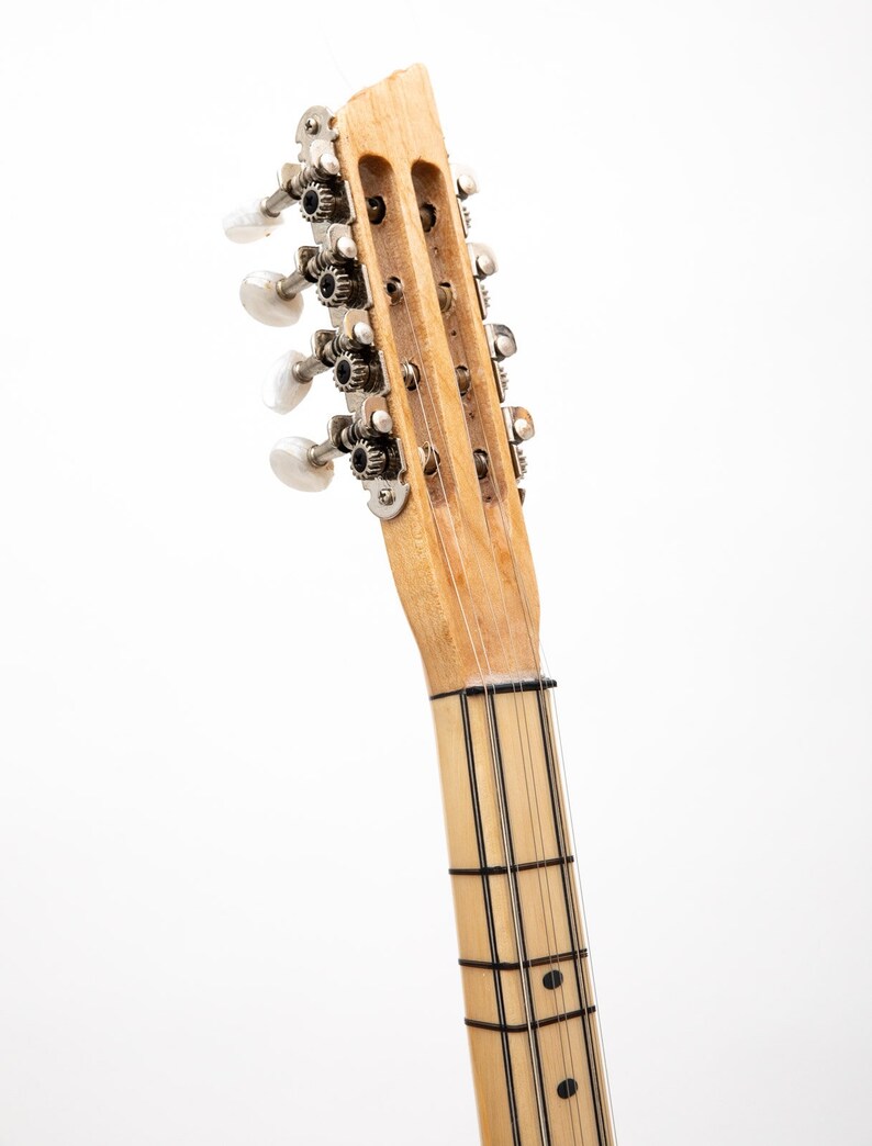 May include: Close-up of the headstock of a wooden stringed instrument with silver tuning pegs. The neck of the instrument has black lines running down the length of the neck.