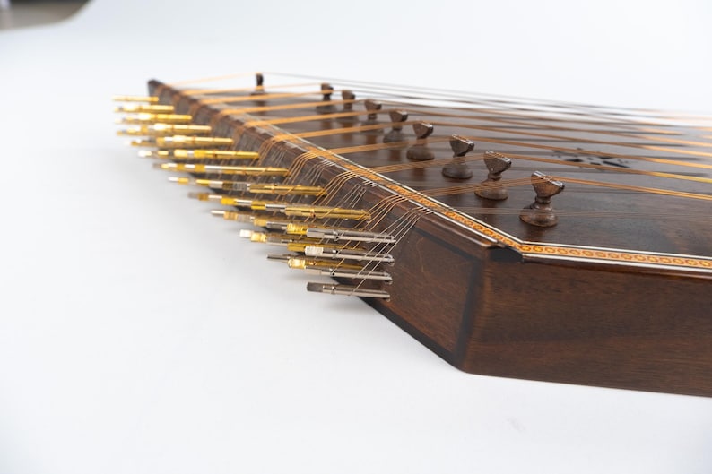 May include: A dark brown wooden santur, a hammered dulcimer, with gold tuning pegs and strings. The instrument has a decorative inlaid border.