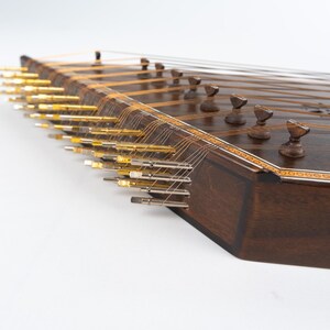 May include: A dark brown wooden santur, a hammered dulcimer, with gold tuning pegs and strings. The instrument has a decorative inlaid border.