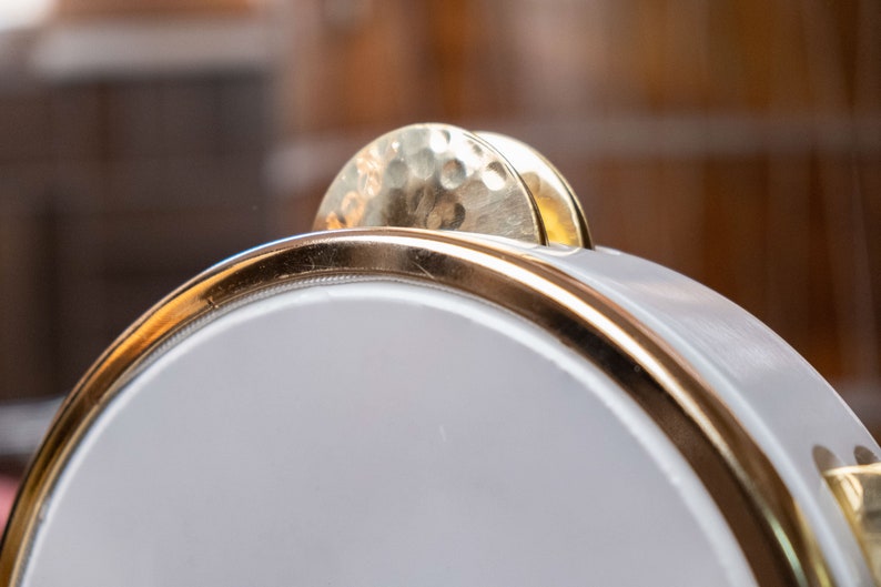 May include: A white tambourine with a gold rim and two gold cymbals on top.