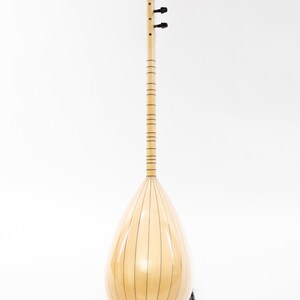 May include: A light wood  saz, a traditional Turkish stringed instrument, with a pear-shaped body and a long neck. The saz is on a black stand and has a natural wood finish.