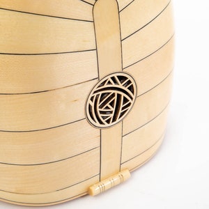 May include: A close-up of the back of a light wood musical instrument with a decorative sound hole. The sound hole is a circle with a geometric design.